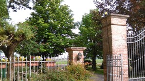 A gated entrance with a brick pillar and a metal gate, surrounded by lush greenery and flowering plants. - B&B Reboglio (Rolo)