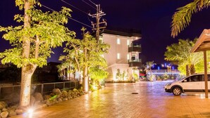 Une cour dallée avec des arbres, une voiture garée et un immeuble doté de balcons.