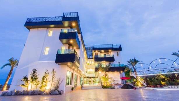 Un hôtel à plusieurs étages doté de balcons, d’une entrée couverte et d’un espace extérieur aménagé avec des palmiers.