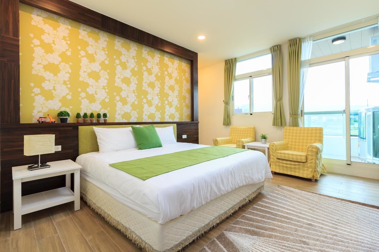 Hotelkamer met een groot bed, nachtkastje, stoel, raam met gordijnen en uitzicht op de stad.