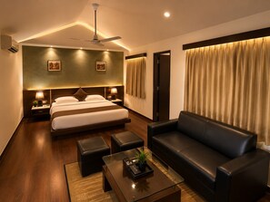 A modern hotel room with a large bed, a leather sofa, a coffee table, and a ceiling fan. - Asiatic Pride Resort (Dhari)