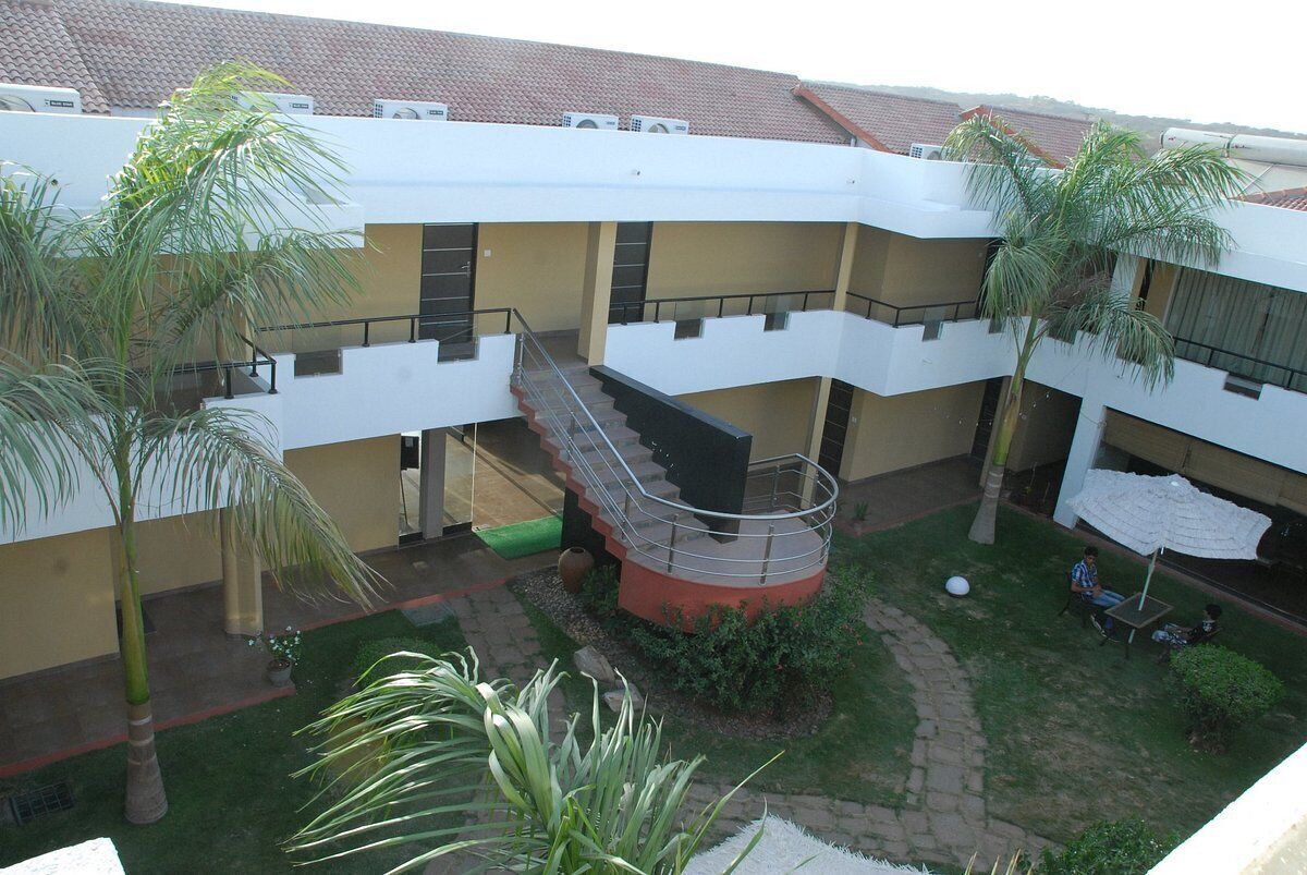 A multi-level building with a central staircase, outdoor seating area, and palm trees.