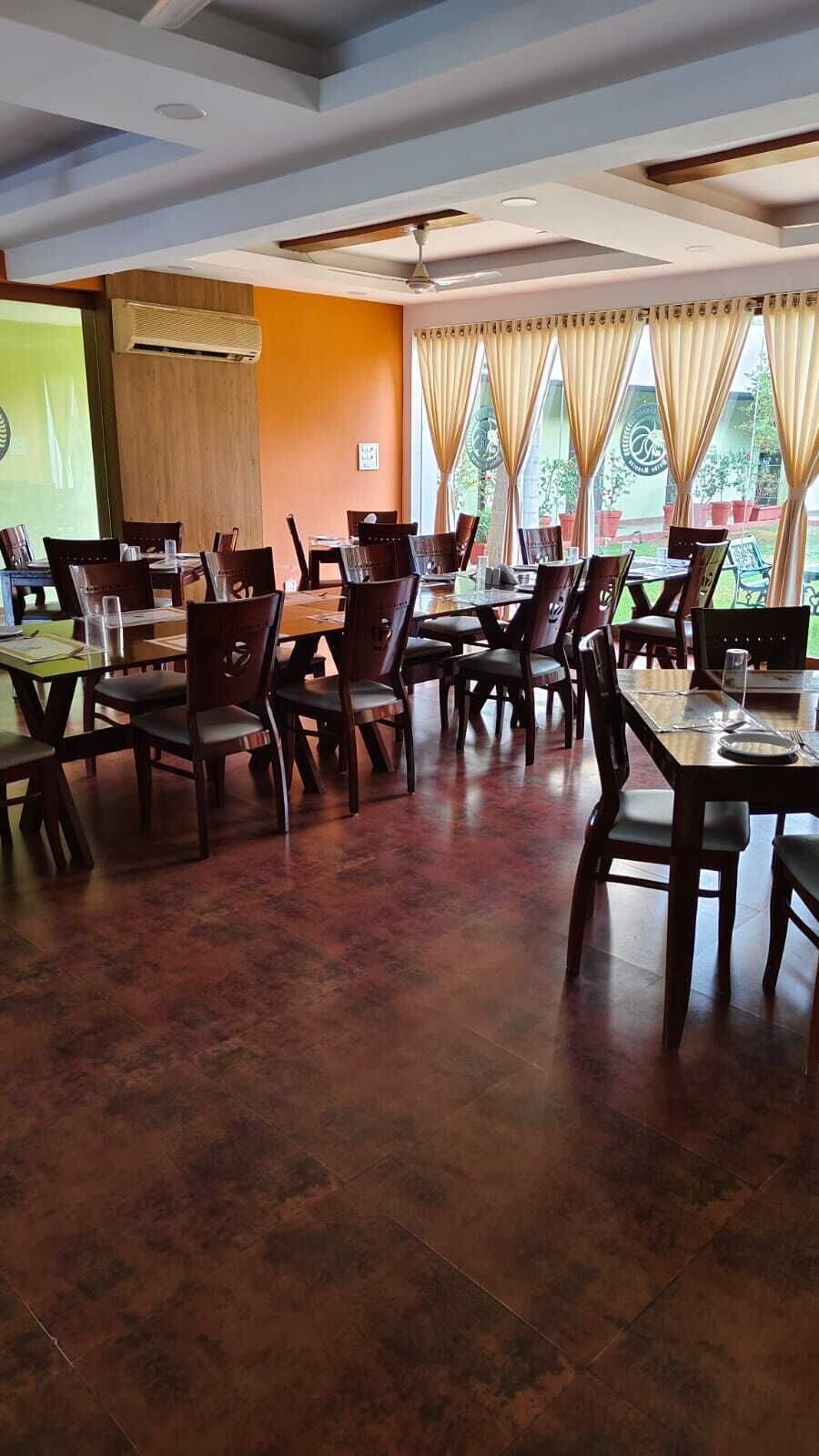 Ein Restaurant mit mehreren Tischen, Stühlen, einem Deckenventilator und großen Fenstern mit Vorhängen.