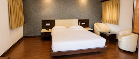 A hotel room with a large bed, a desk, two chairs, and a wall-mounted air conditioning unit.