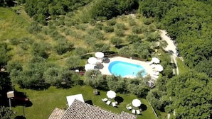An aerial view of a property with a swimming pool surrounded by lush greenery, a patio area with white umbrellas, and a small deck. - Agriturismo Le Dolci Colline (Valfabbrica)