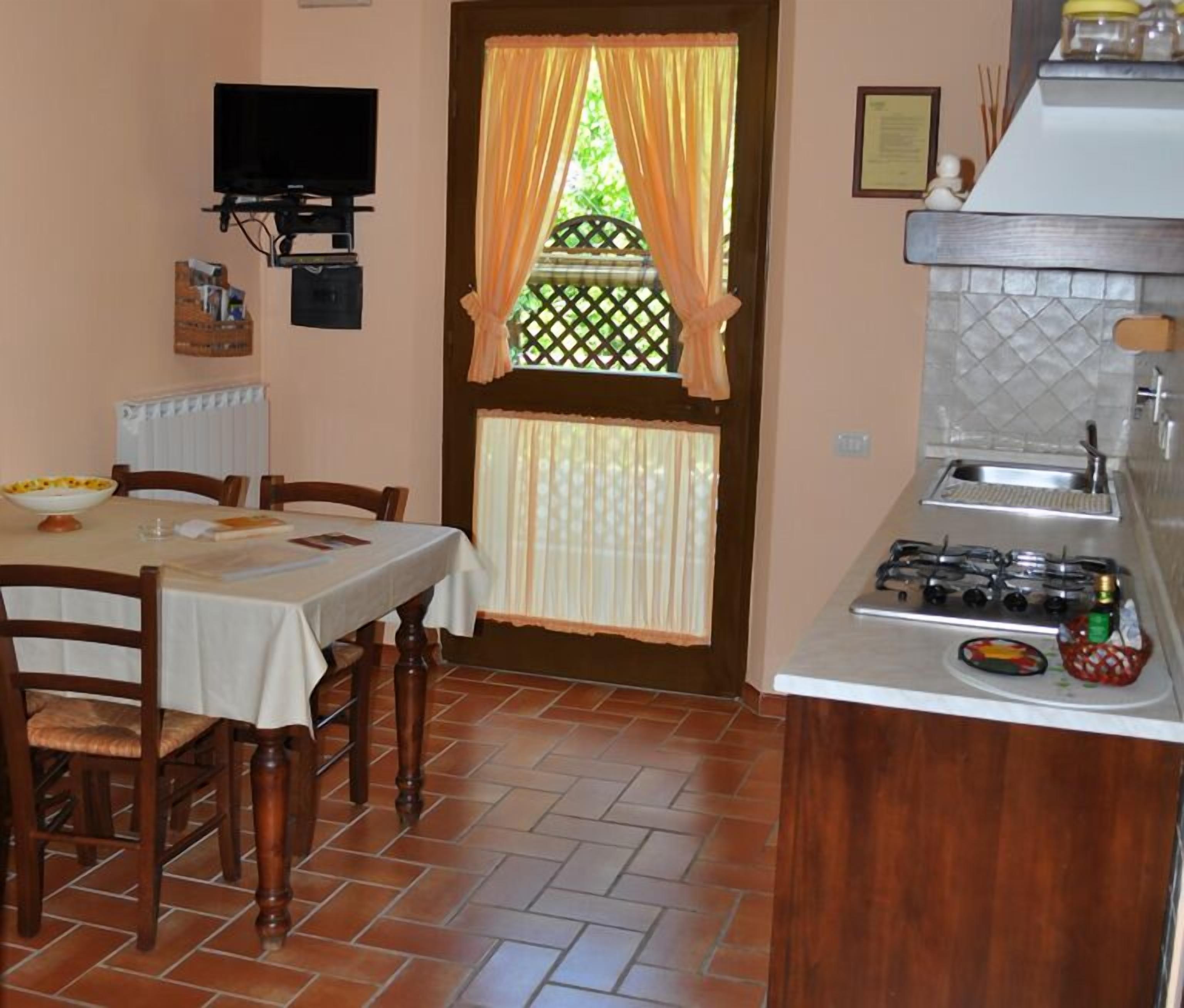 Cozinha compacta com fogão a gás, mesa de jantar com cadeiras e janela com cortinas.