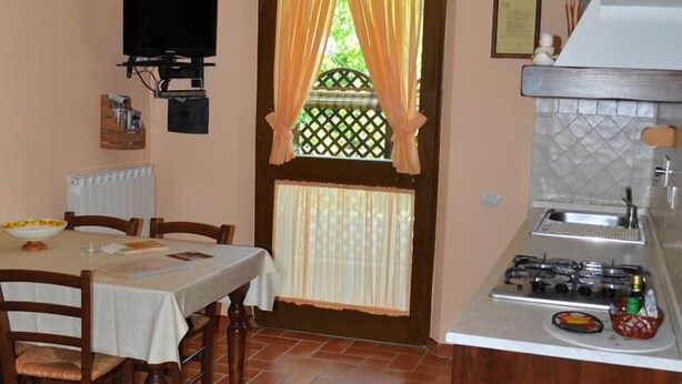 A compact kitchen with a gas stove, a dining table with chairs, and a window with curtains. - Agriturismo Le Dolci Colline (Valfabbrica)