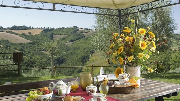 A picnic setup on a wooden table with a red cloth, surrounded by a scenic view of rolling hills and a clear sky. - Agriturismo Le Dolci Colline (Valfabbrica)