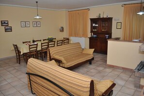 A living room with striped sofas, a dining table with chairs, a kitchen area with a cabinet, and a radiator. - Agriturismo Le Dolci Colline (Valfabbrica)