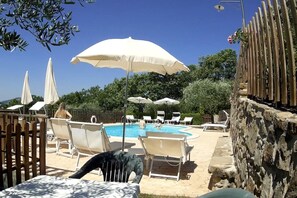 A poolside area with lounge chairs and umbrellas, a stone wall, and a clear blue sky. - Agriturismo Le Dolci Colline (Valfabbrica)