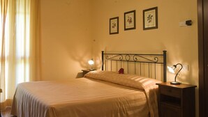 A neatly made bed with a headboard, a bedside table with a lamp, and three framed pictures on the wall. - Agriturismo Le Dolci Colline (Valfabbrica)