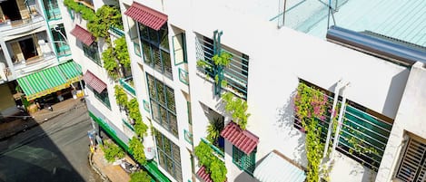 Un edificio de varios pisos con balcones, plantas verdes y vista a la calle.