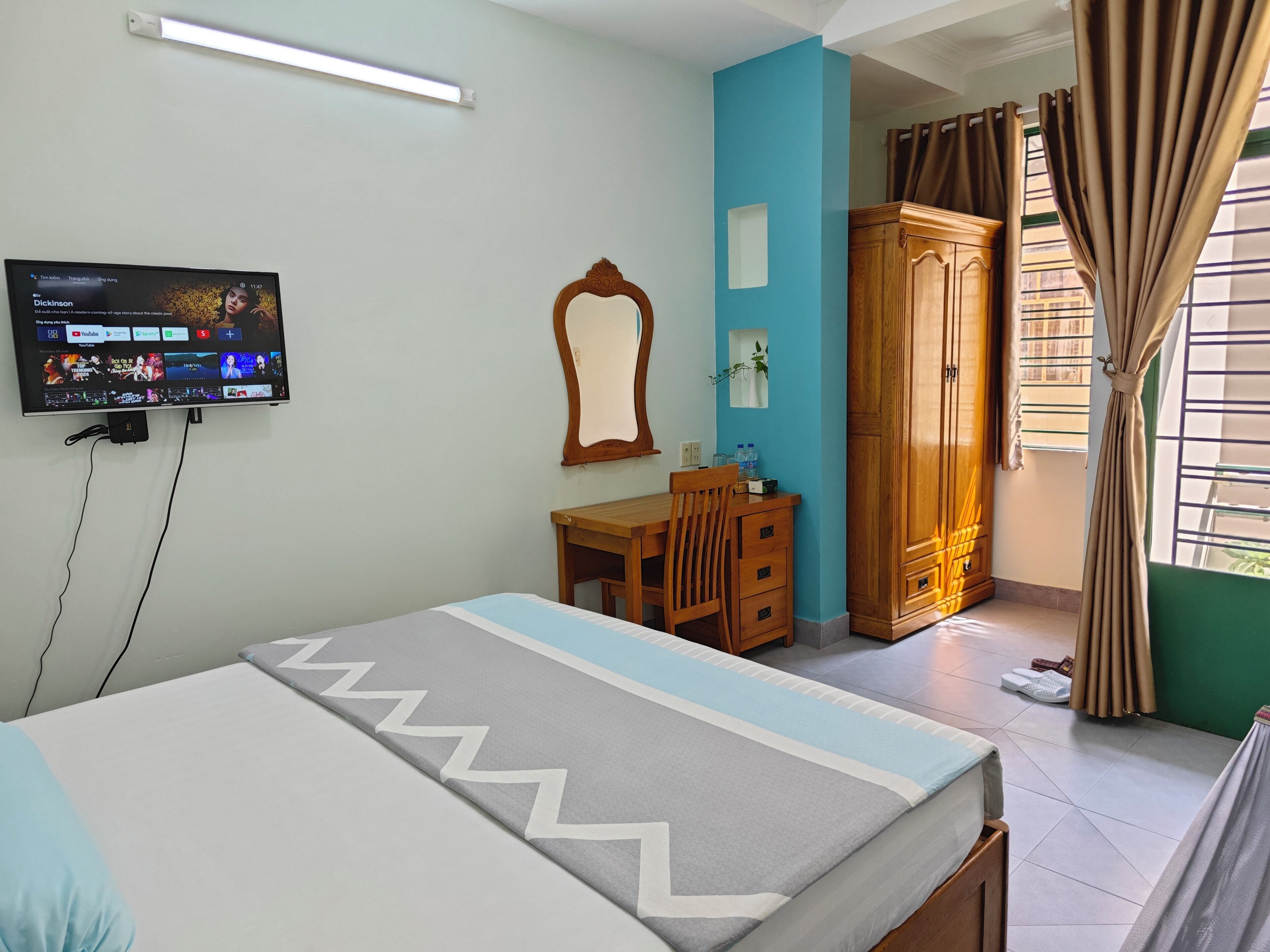 A hotel room with a bed, a desk, a mirror, a wardrobe, and a TV displaying a YouTube channel.