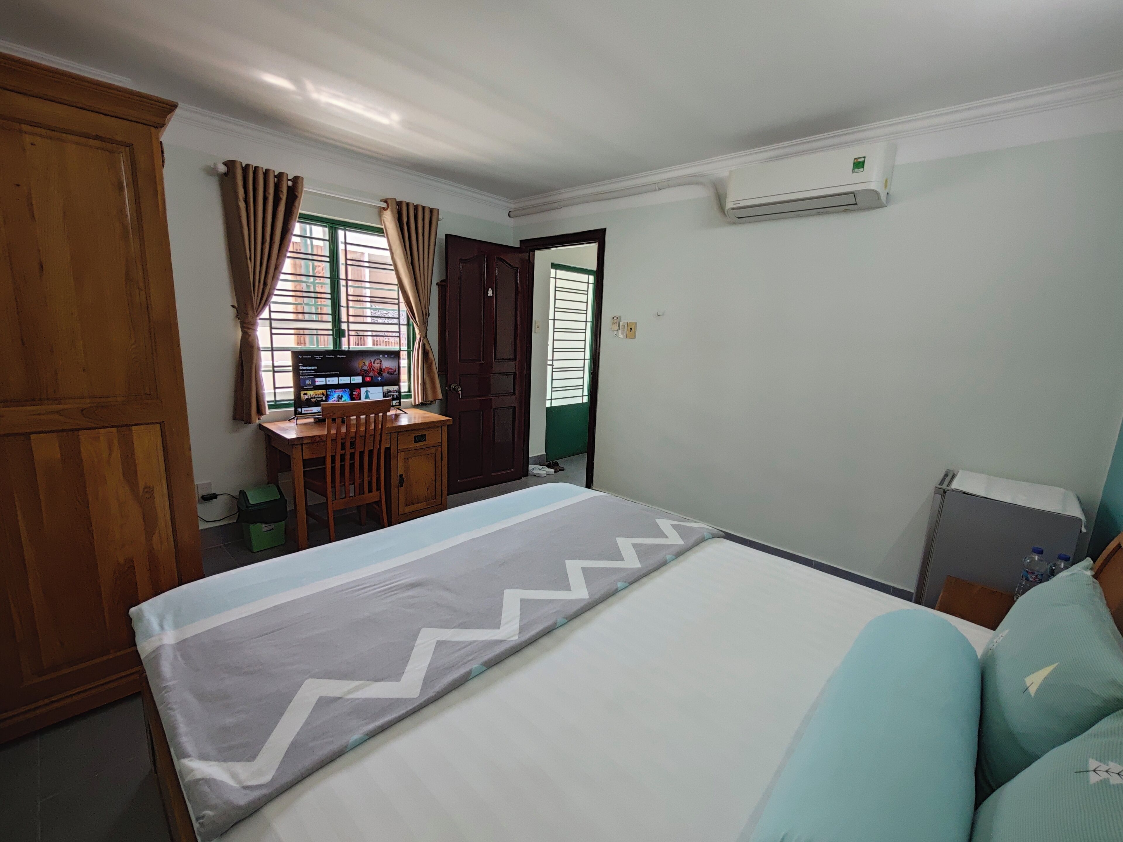 A bedroom with a bed, a desk with a computer, a wardrobe, and an air conditioning unit.
