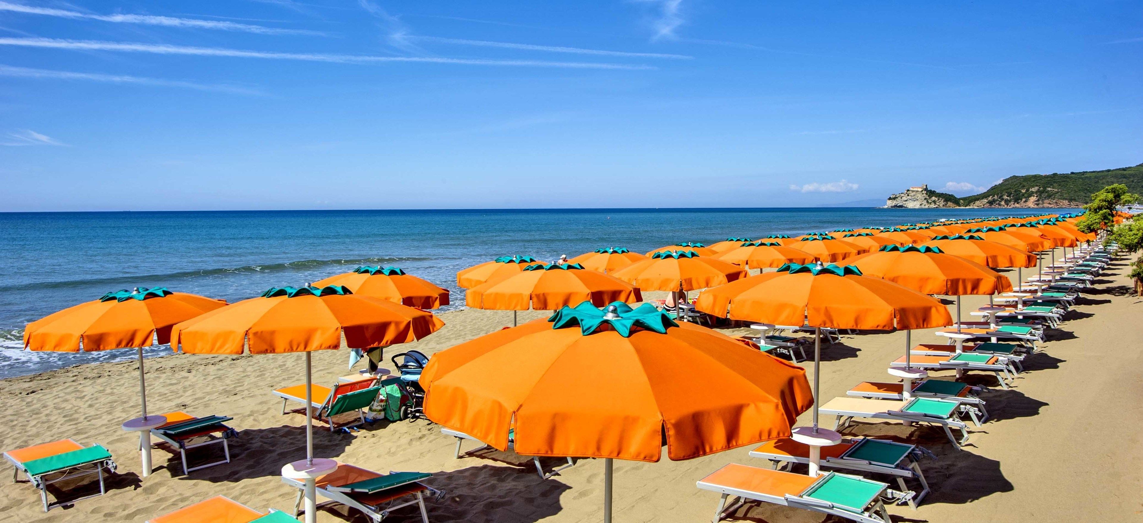 Une plage bordée de rangées de parasols orange et de chaises longues vertes.