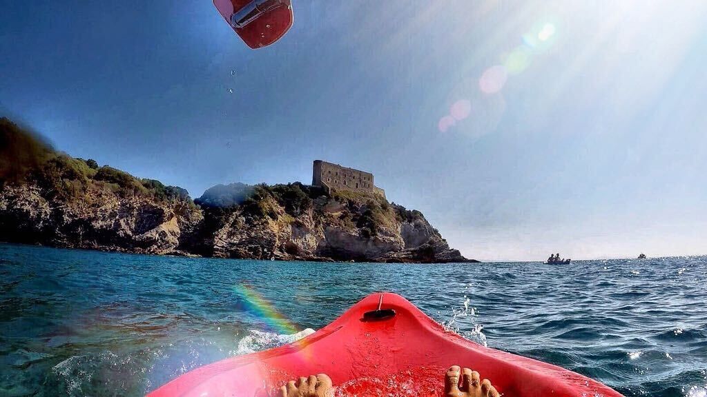 Un kayak rouge sur une eau calme, avec un château perché sur une falaise rocheuse en arrière-plan.