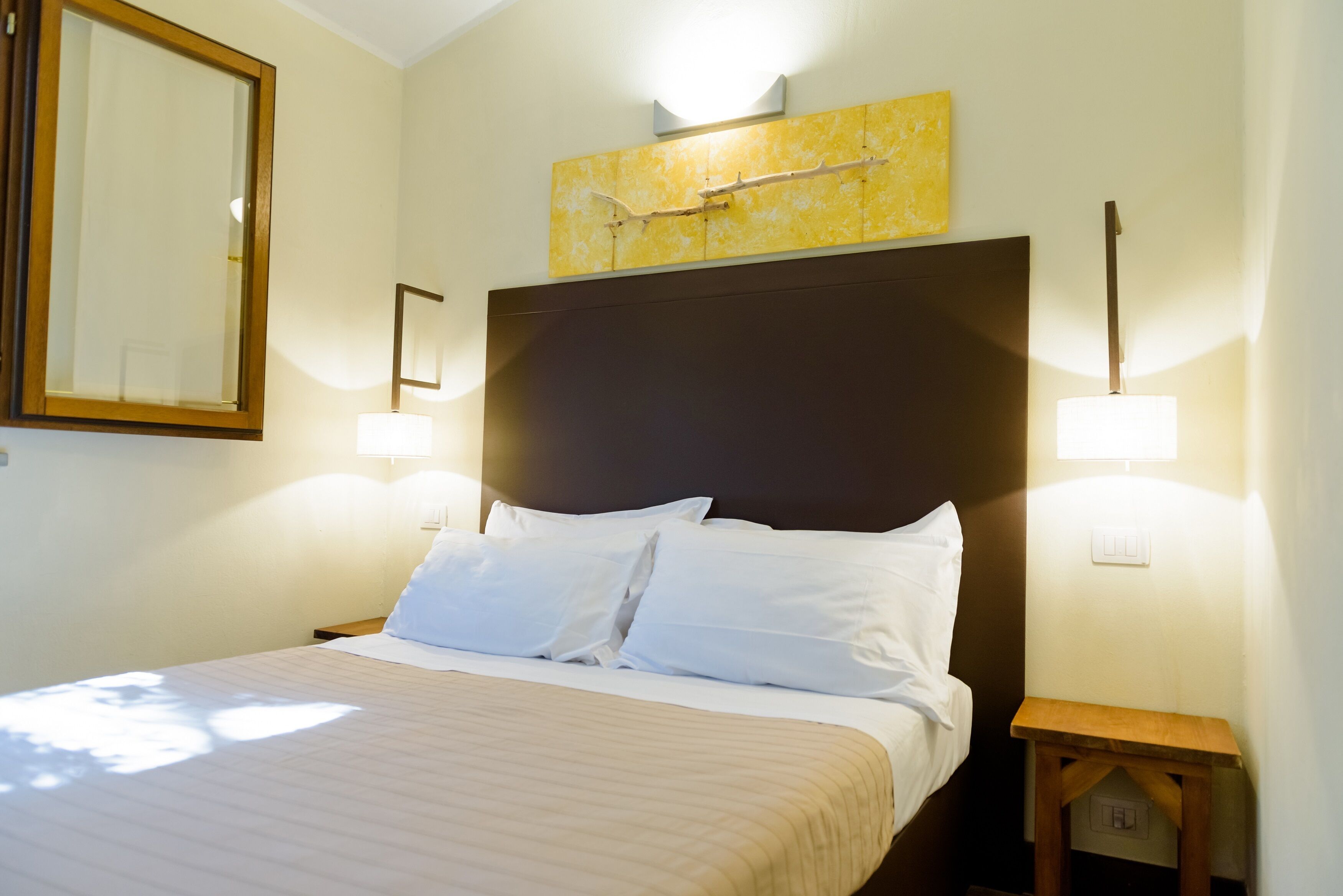 A neatly made bed with white linens, a wooden headboard, and two bedside lamps.