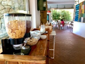 Una barra de desayuno con dispensadores de cereales y leche, una jarra y una cesta de bolsas de papel.