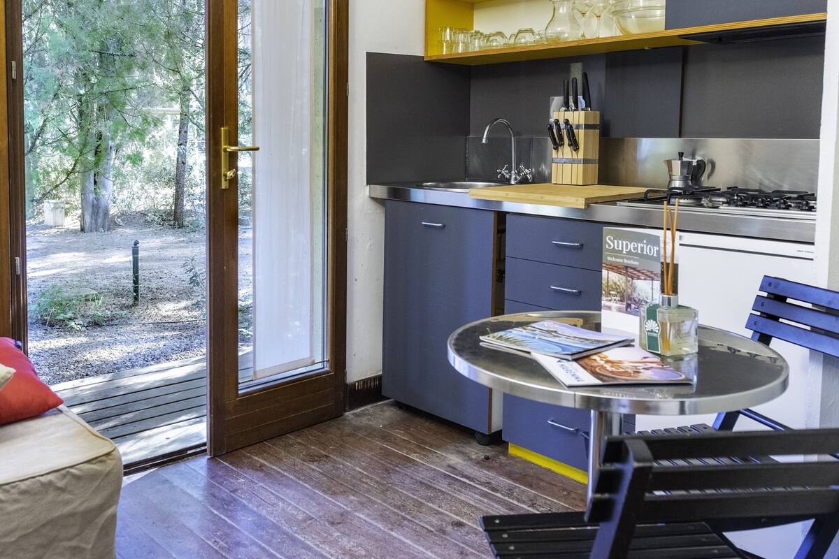A compact kitchen with a dining area, a view through the glass door, and a small table with a magazine.