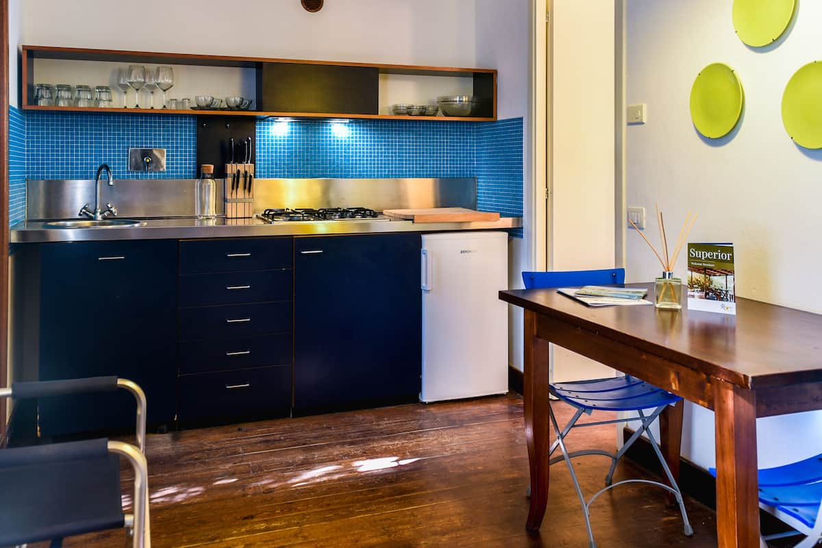 A compact kitchen with a sink, stove, and cabinets, a dining table with chairs, and a wall with decorative plates.