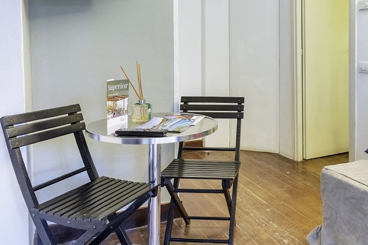 A small room with a round table, two chairs, a sofa with cushions, and a door.