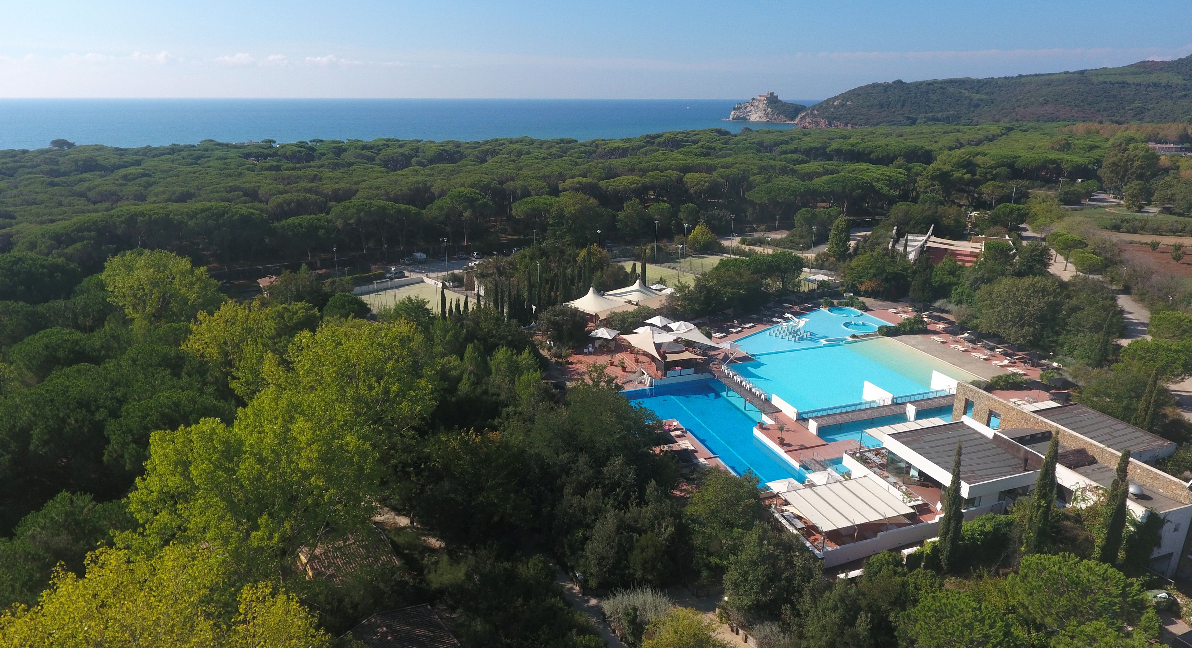 Vista aérea de un resort con una amplia piscina, abundante vegetación y una lejana vista al mar.