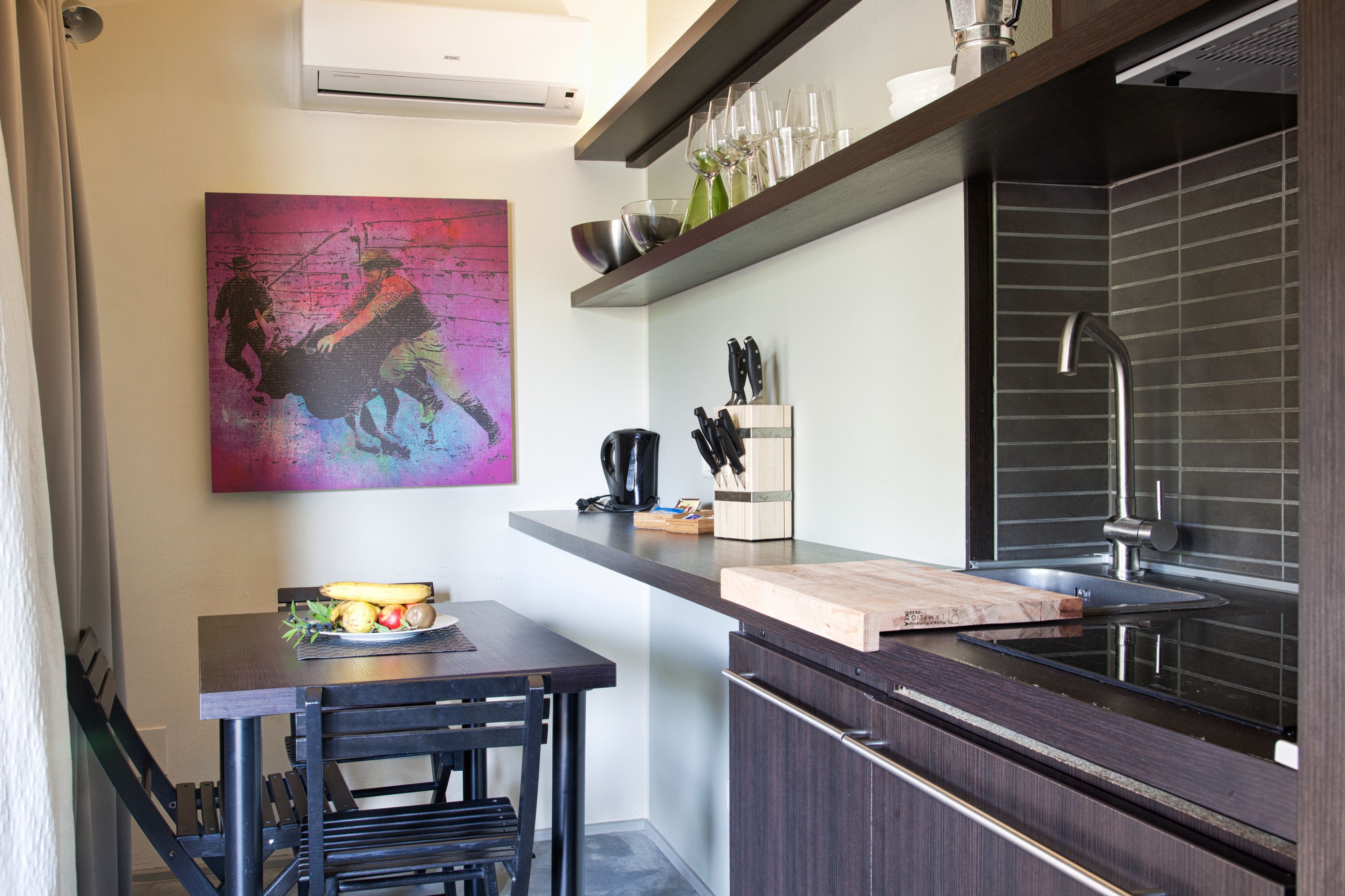 Een moderne keuken met een donker aanrecht, een gootsteen en een messenblok. Er hangt een schilderij aan de muur en boven de gootsteen is een raam.