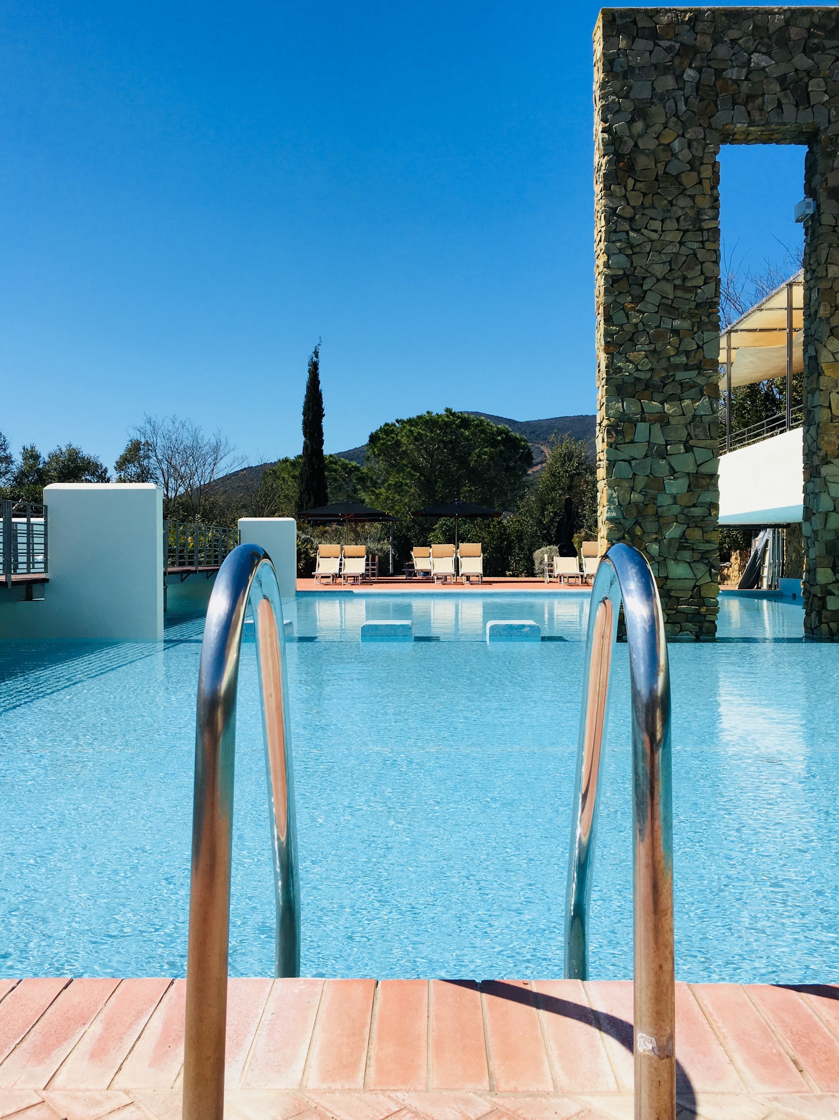 A clear blue pool with a stone archway and metal poolside railings.