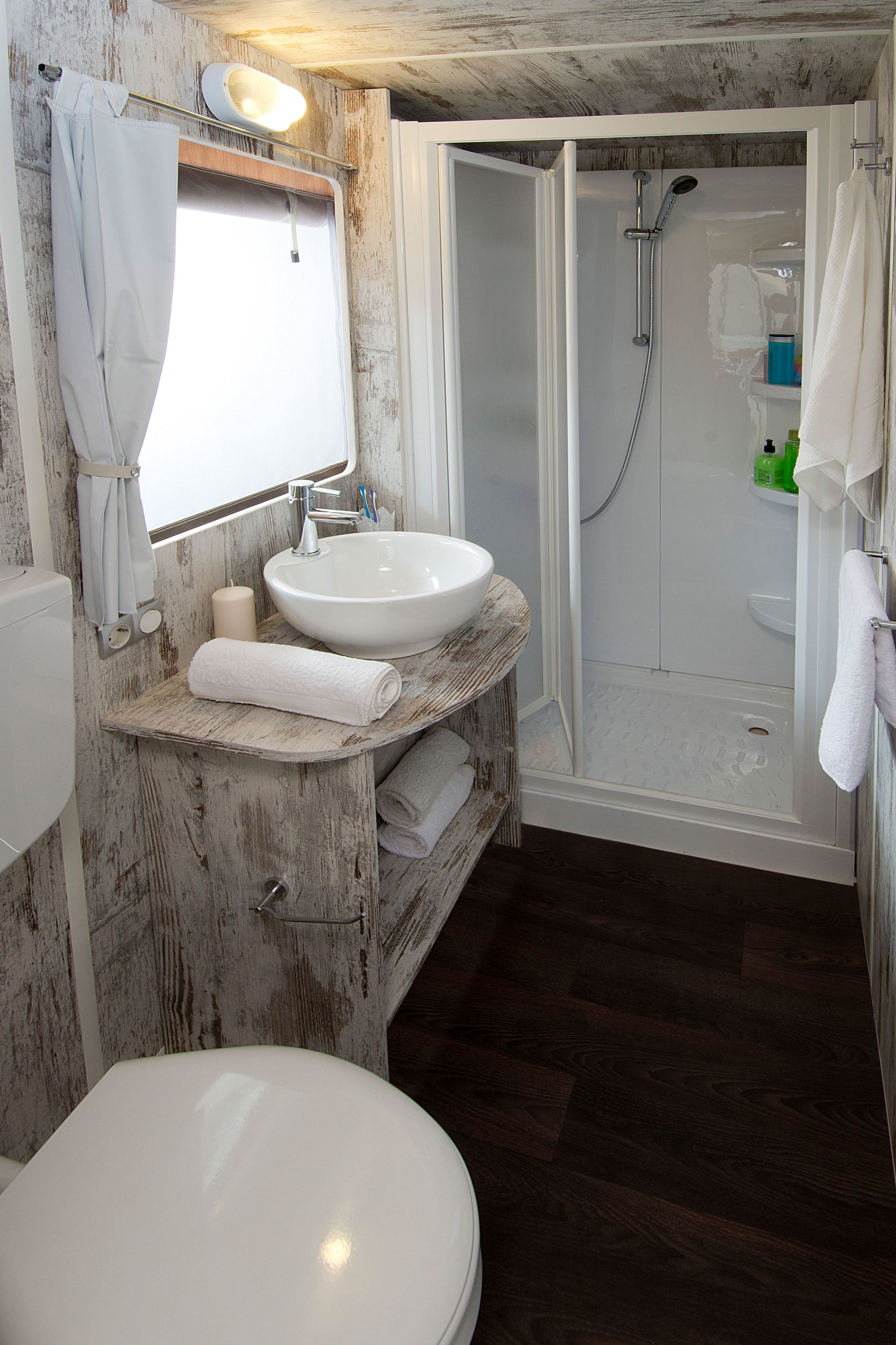 A bathroom with a white sink, mirror, and toilet. There is a shower area with a glass door and a towel rack.