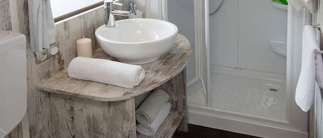 A bathroom with a white sink, mirror, and toilet. There is a shower area with a glass door and a towel rack.