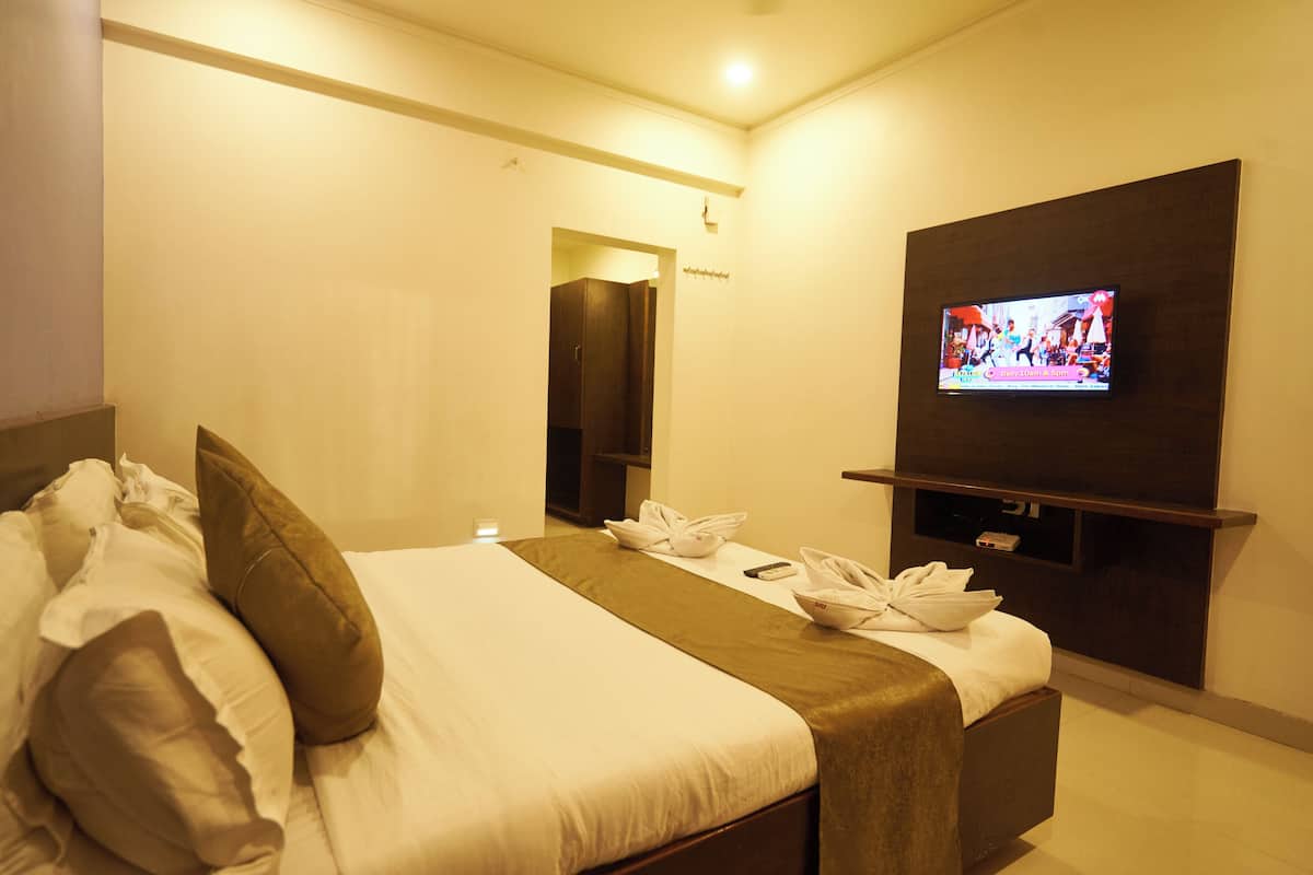 A hotel room with a bed, a TV mounted on the wall, and a small table with a remote control.