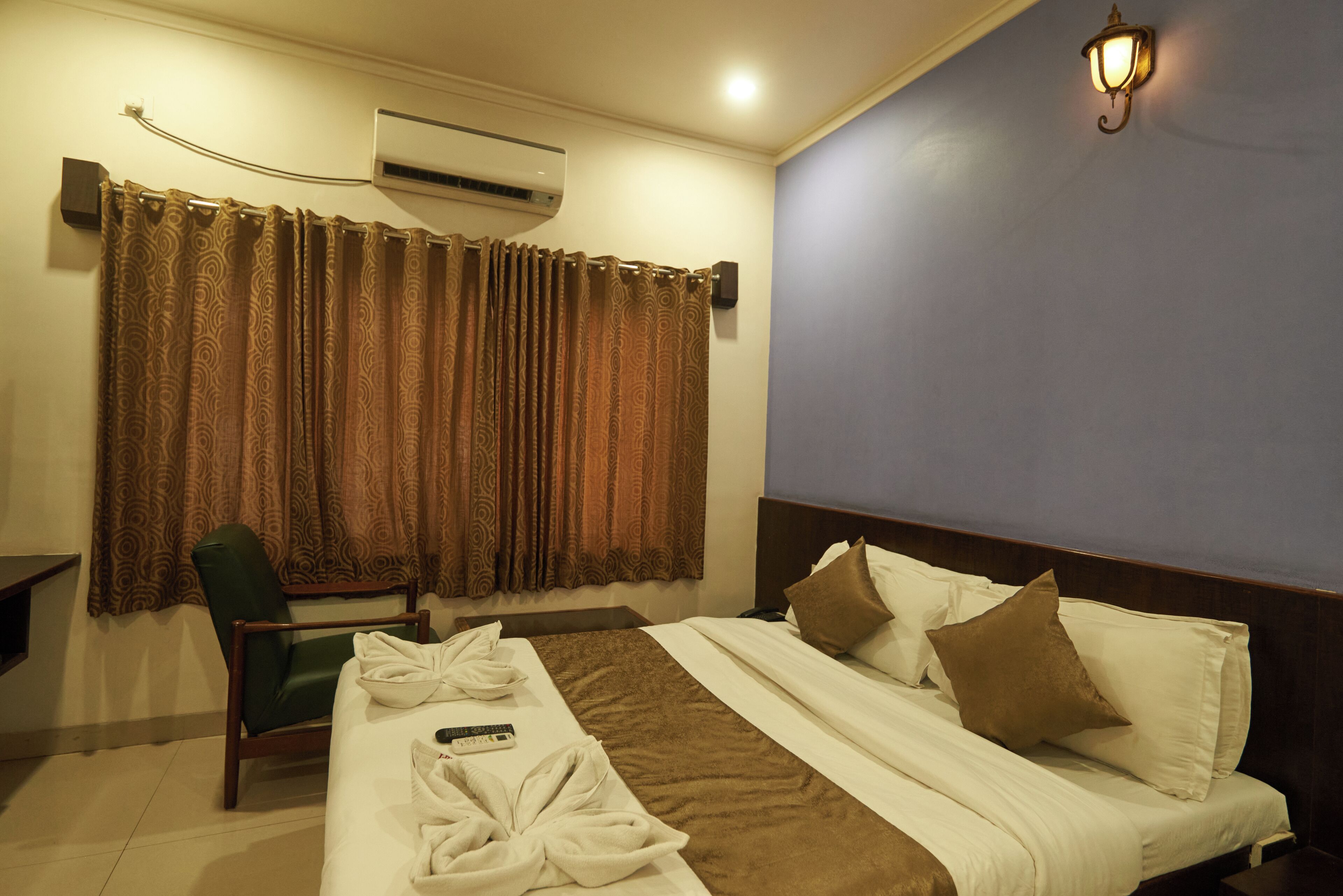 A hotel room with a bed, a chair, a remote control, and a curtain.