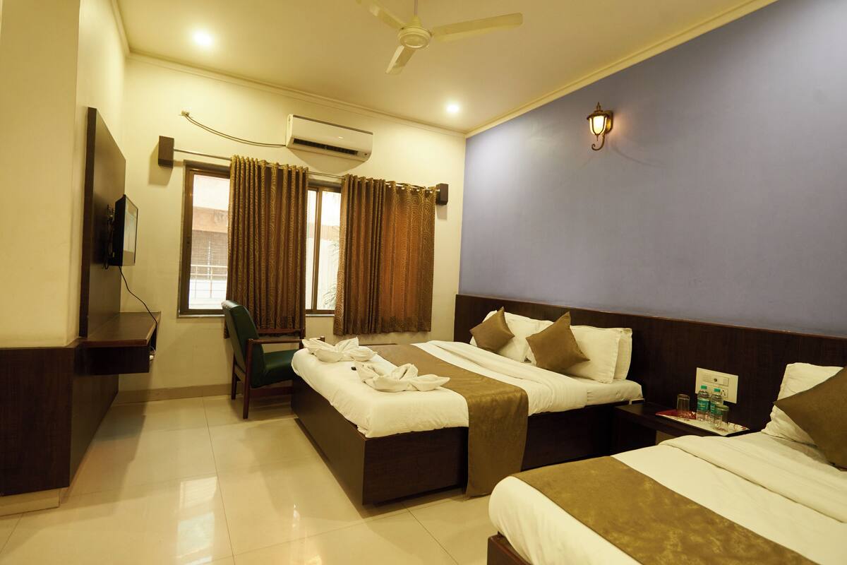 A hotel room with two beds, a desk, a chair, an air conditioning unit, and a window with curtains.