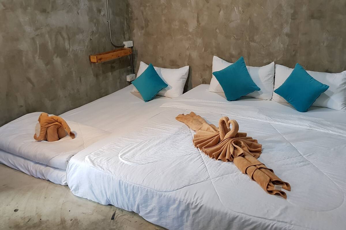 Uma cama com roupa de cama branca, almofadas verde-água e uma toalha disposta em formato de cisne.