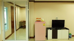 A compact living space with a sliding glass door leading to a hallway, a small pink refrigerator, a black TV stand, and a white cabinet. - Tree House Chachoengsao (Chachoengsao)