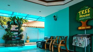 A reception area with a blue wall, a wooden bench, a small table, and a plant arrangement. - Tree House Chachoengsao (Chachoengsao)