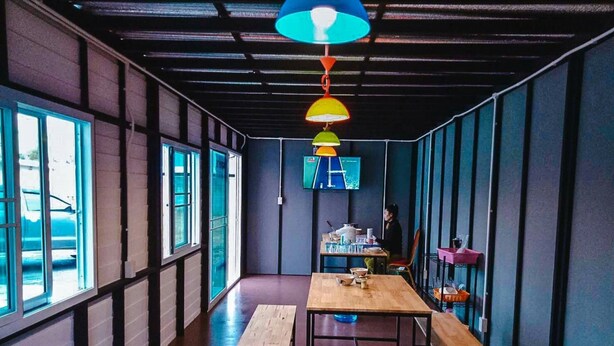A modern interior with wooden tables and benches, large windows, and colorful pendant lights. - Tree House Chachoengsao (Chachoengsao)