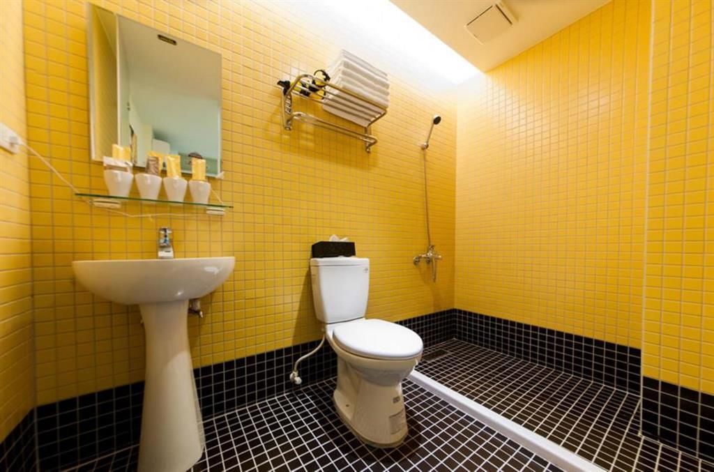 A bathroom with yellow tiled walls, a white sink, a toilet, and a shower area.