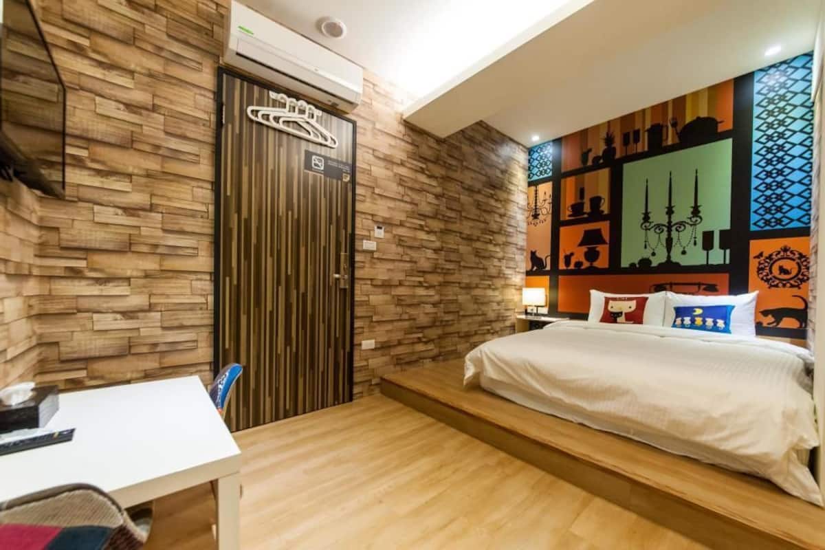A hotel room with a wooden wall, a bed with white bedding, a desk with a chair, and a wall with decorative patterns.