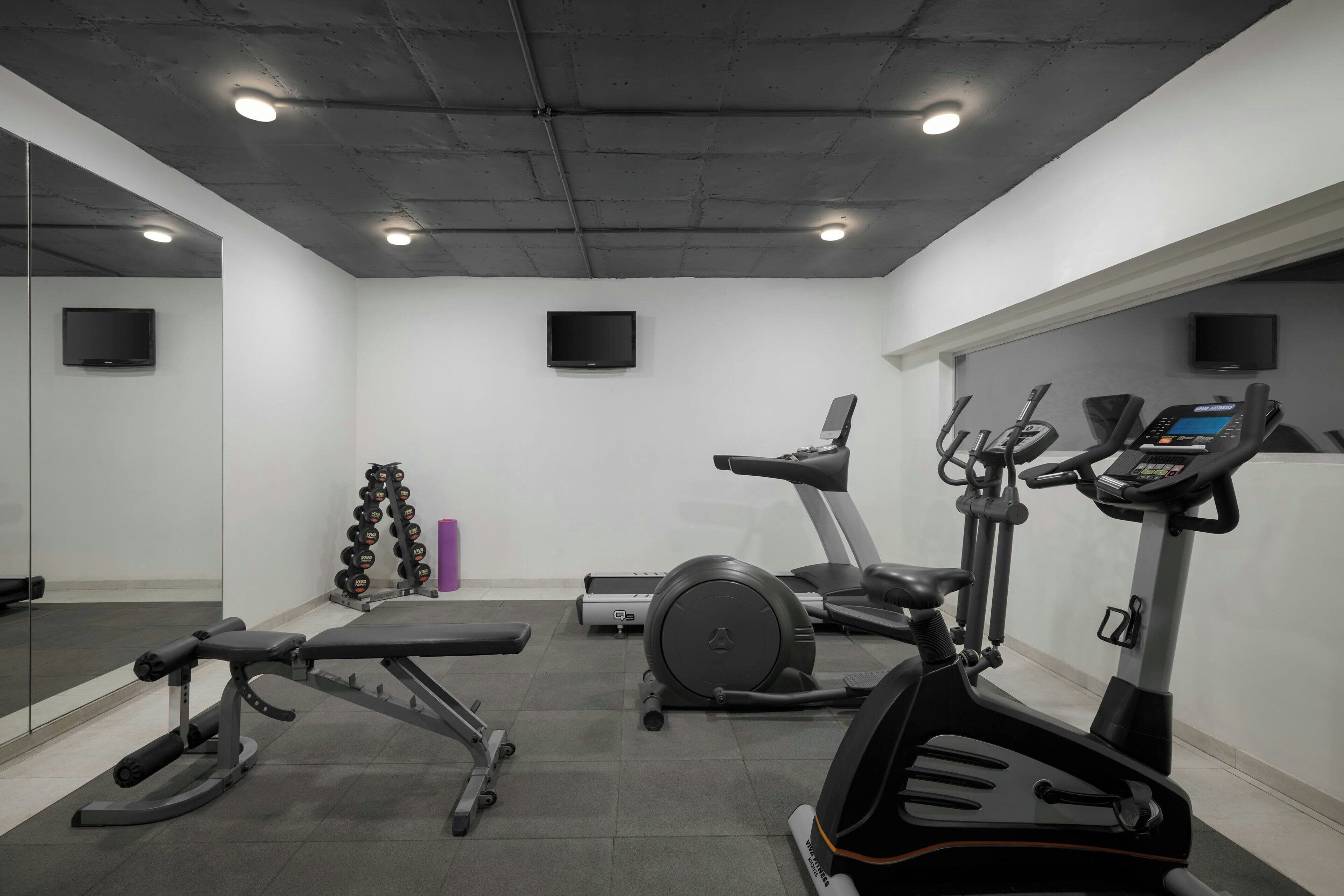 A gym with exercise equipment, including treadmills and weight machines, and a television mounted on the wall.
