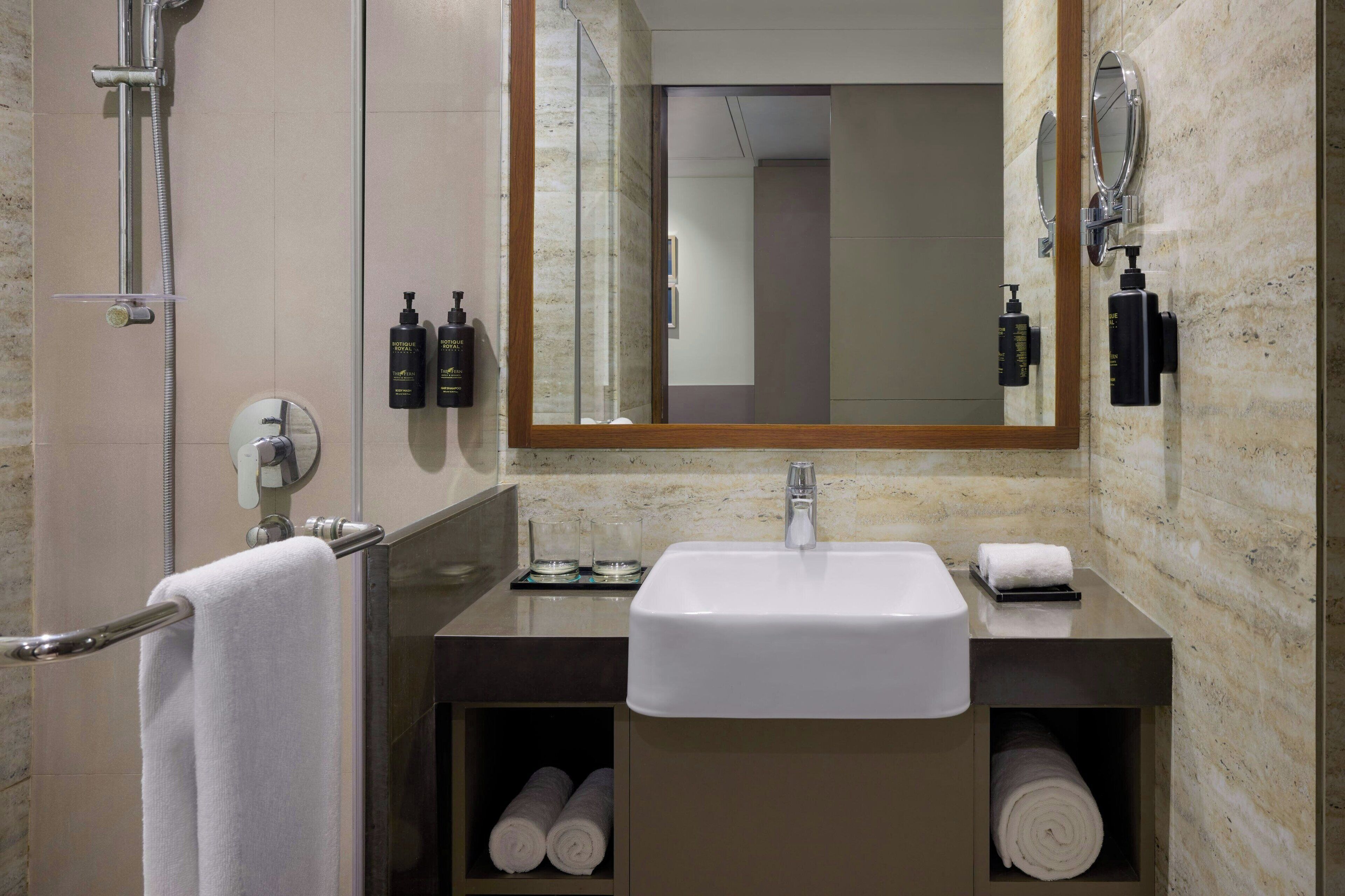 Een moderne badkamer met een wastafel, spiegel, handdoekhouder en douche.
