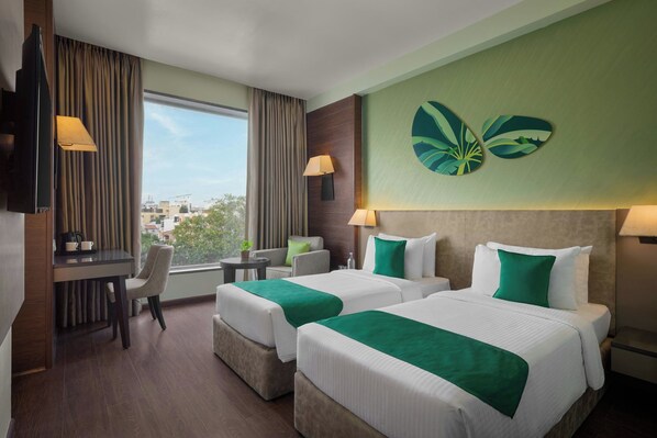 A hotel room with two beds, a desk, a chair, a TV, and a window with a view of buildings. - The Fern Vadodara, Series by Marriott (Vadodara)