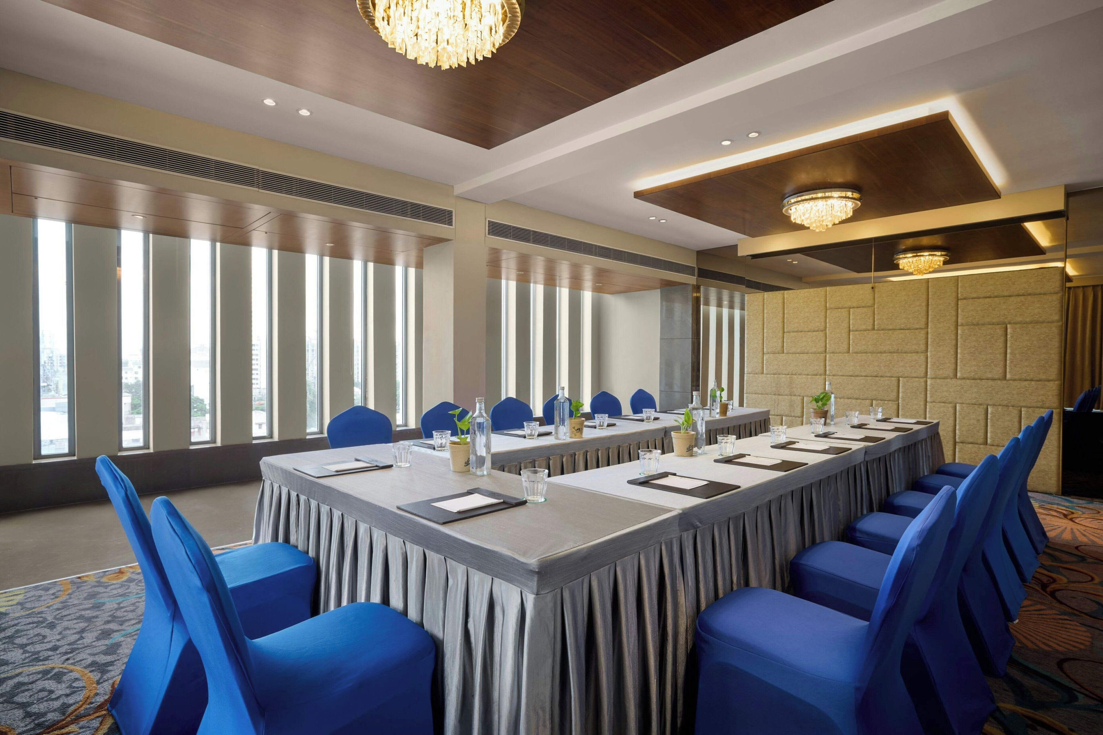 A conference room with a long table, blue chairs, and large windows.