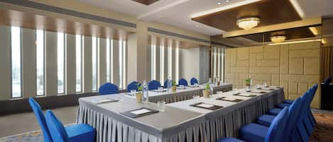 Un salón de conferencias con una larga mesa, sillas azules y ventanas amplias.