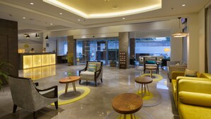 Um saguão de hotel moderno com balcão de recepção, áreas de estar e vista para o exterior.