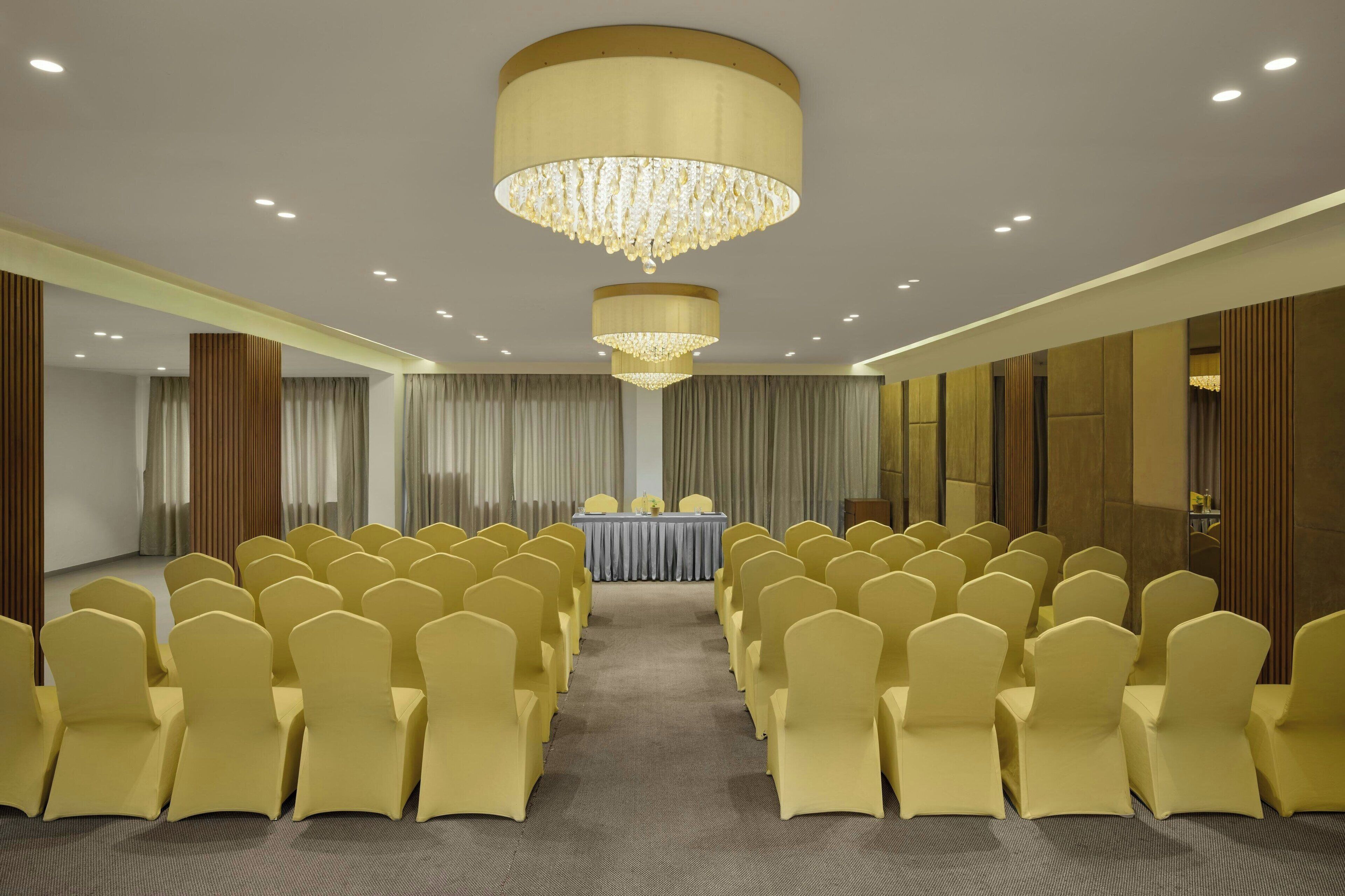 A conference room with rows of yellow chairs, a table with a blue tablecloth, and a large chandelier.