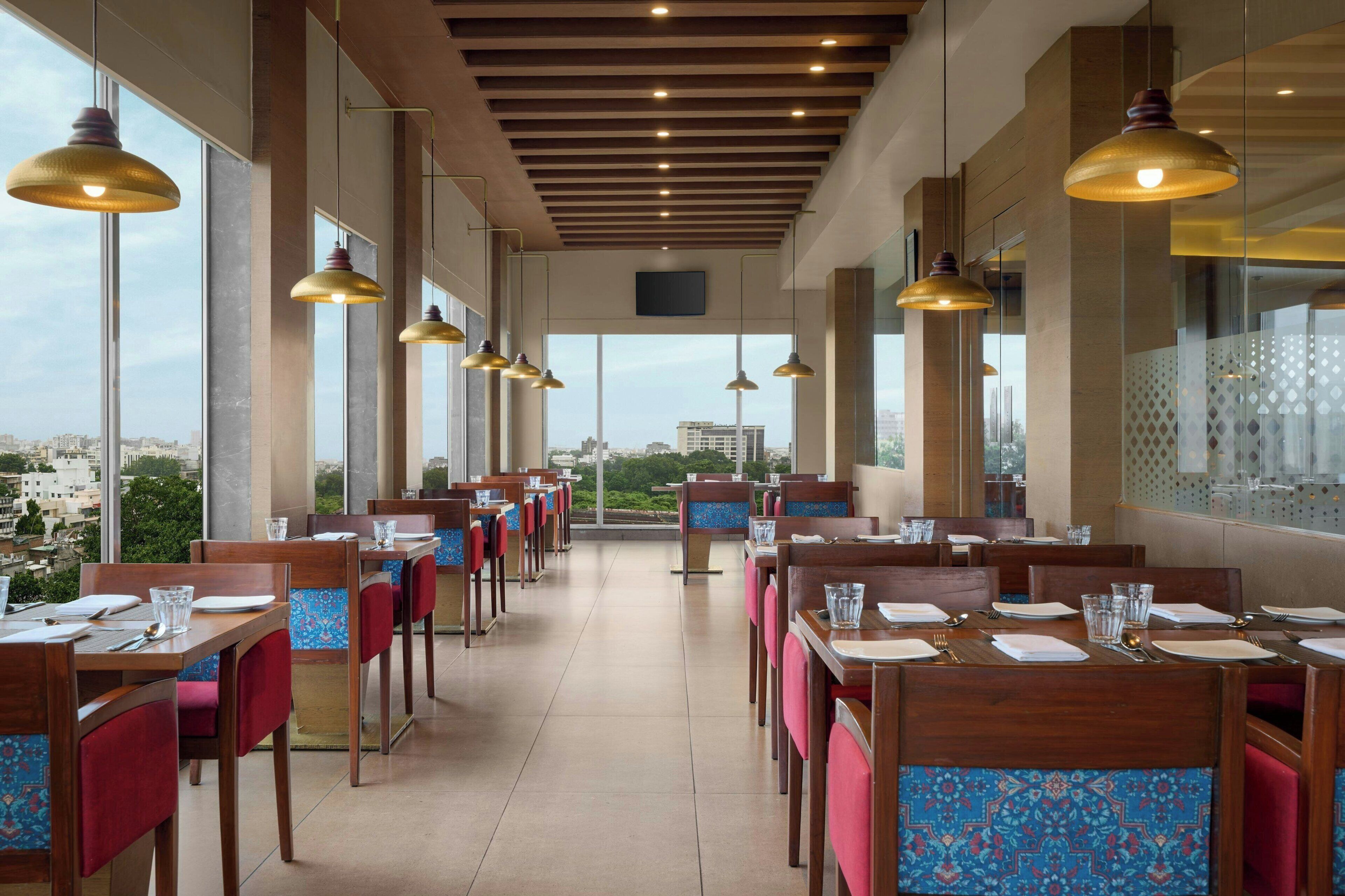 A restaurant with tables and chairs, large windows, and hanging pendant lights.