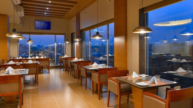 Restaurante com várias mesas e cadeiras, janelas amplas e luminárias pendentes.