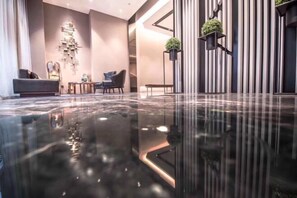 A modern lobby with a reflective floor, a seating area with sofas and a coffee table, and vertical striped walls with potted plants.