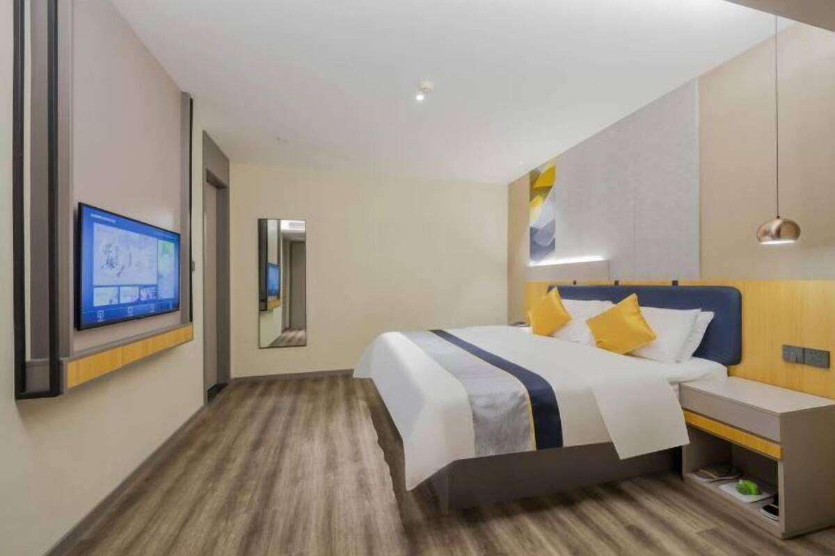 A modern hotel room with a bed, bedside table, TV, and a mirror.